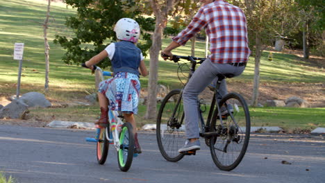 father and daughter riding bikes together in a park, pan