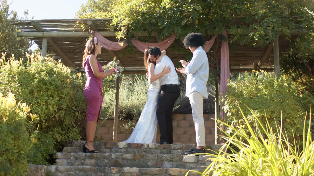 Novios intercambiando anillos, abrazándose y posando bajo una pérgola con cortinas, celebrando su boda