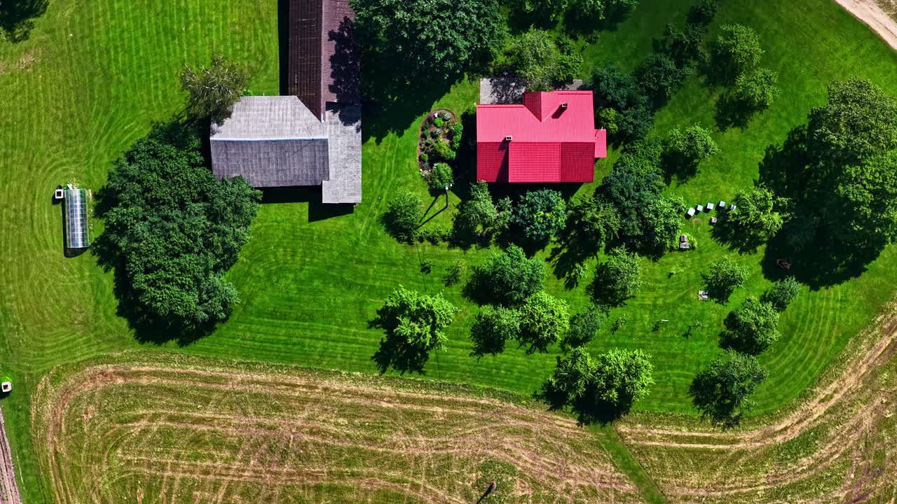 En top-down luft-timelapse viser en person med en plæneklipper, der klipper den store, grønne have på en smuk landejendom med rødt tag i Letland
