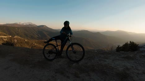 Niña-Montando-Su-Bicicleta-Y-Deteniéndose-En-Una-Montaña-Al-Atardecer