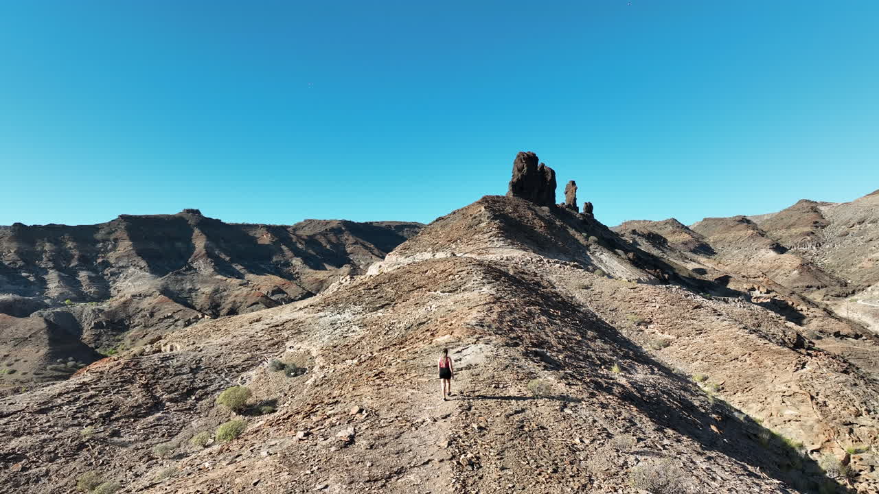 seguimiento aéreo de una mujer joven con el pelo largo que se dirige hacia una gran formación rocosa cerca de la playa medio almud en la isla de gran canaria