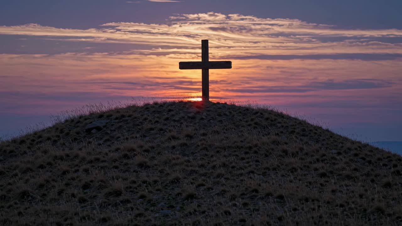 Silhouette of a cross on a hill at sunset, captured from a low angle, emphasizing the sky's colors