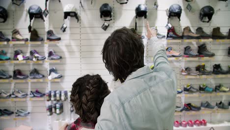 Rear-view-of-a-man-and-woman-choosing-shoes-for-hiking-standing-in-front-beautiful-showcase-on-the-background