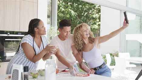 diversos amigos toman una selfie en una cocina de casa brillante mientras hacen pizza