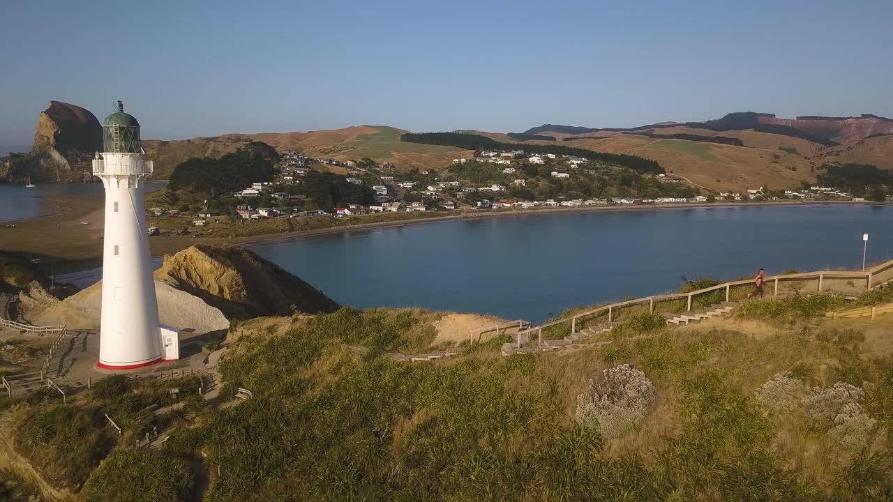 하얀 등대에서 멀리 떨어진 통로를 뛰어가는 여성의 측면 공중 샷