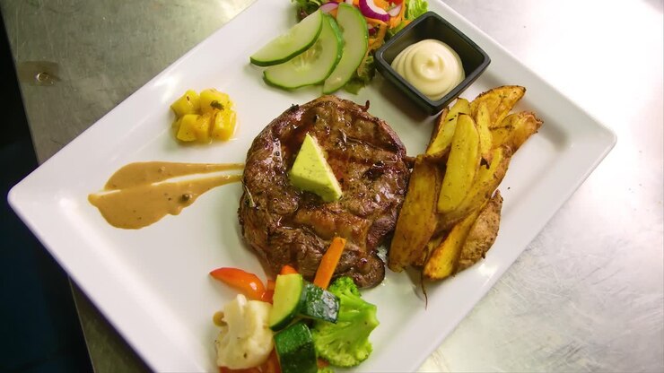 Bistec perfectamente a la parrilla con mantequilla de ajo, patatas horneadas tipo steak fries y ensalada fresca de jardín.