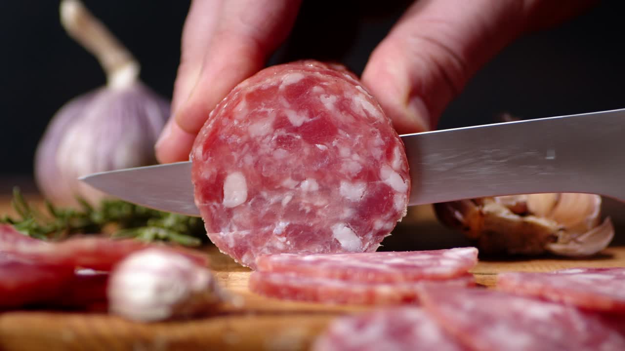 mano masculina con un cuchillo corta un pedazo de salami.