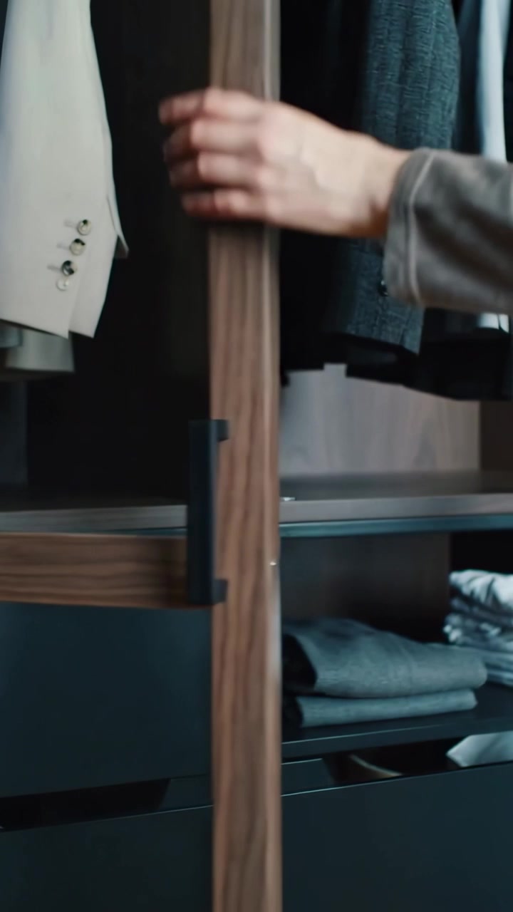 Video vertical: Torso con conjunto gris agarrando las manijas y abriendo una puerta corredera de armario, mostrando un blazer.