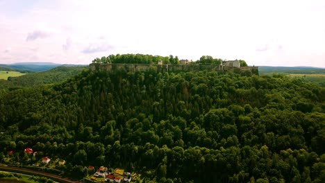 drone at high altitude approaches castel on the hill with trees rocks and green fields surrounding the scenery in europe