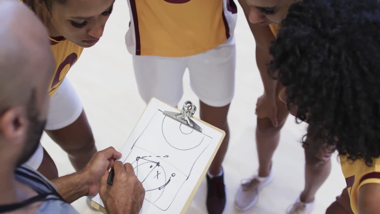una squadra di basket femminile felice e diversificata che si allena con un allenatore maschio in un campo coperto, al rallentatore