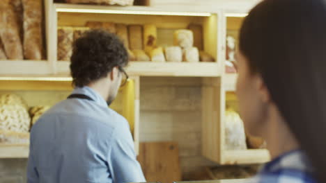 Close-Up-Of-The-Handsome-Male-Vendor-In-The-Bakery-Shop-Talking-With-The-Young-Woman-Who-Buying-Bread