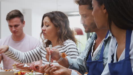 grupo de hombres y mujeres sentados alrededor de una mesa comiendo la comida que han preparado en la clase de cocina