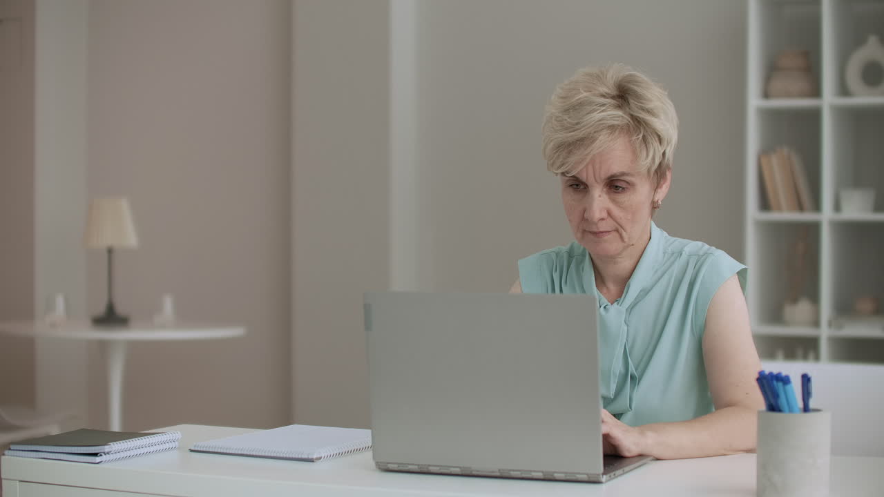 retiree woman is typing on laptop female writer is working and writing at home looking at display with concentration