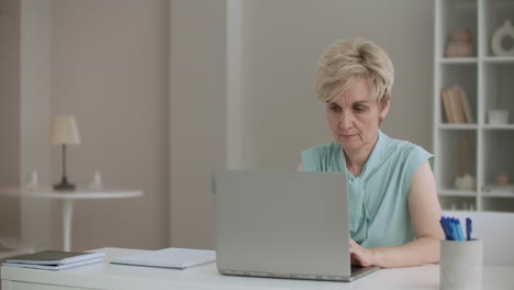 una mujer jubilada está escribiendo en una computadora portátil. una escritora está trabajando y escribindo en casa mirando la pantalla con concentración.