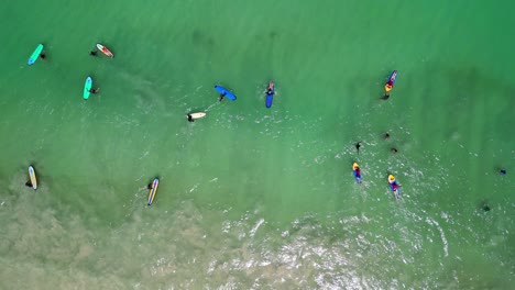 aerial of surfers with colorful surfboards in the green ocean of selong belanak beach, indonesia