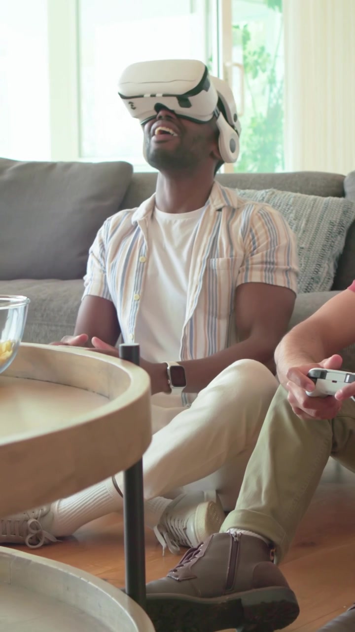 Video verticale: Un uomo in camicia a righe reagisce alle cuffie, ride e condivide bottiglie mentre gioca a casa.
