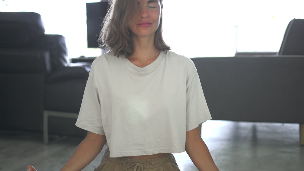 View close up of happy smiling woman with closed eyes sitting in lotus pose in living room