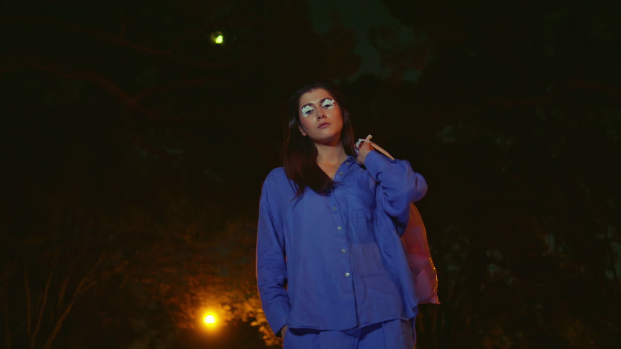 mujer de moda sosteniendo una bolsa de basura después de la limpieza del parque bajo el resplandor de la linterna nocturna