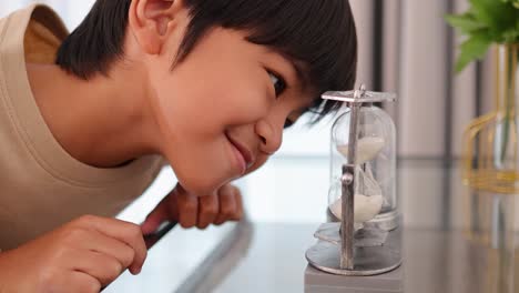 A child intently watches sand flow through an hourglass, showcasing curiosity and fascination in a softly lit room