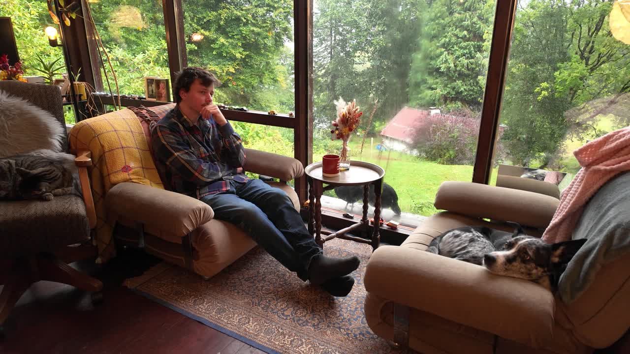 Young Man sitting on armchair with dog in cabin surrounded by nature
