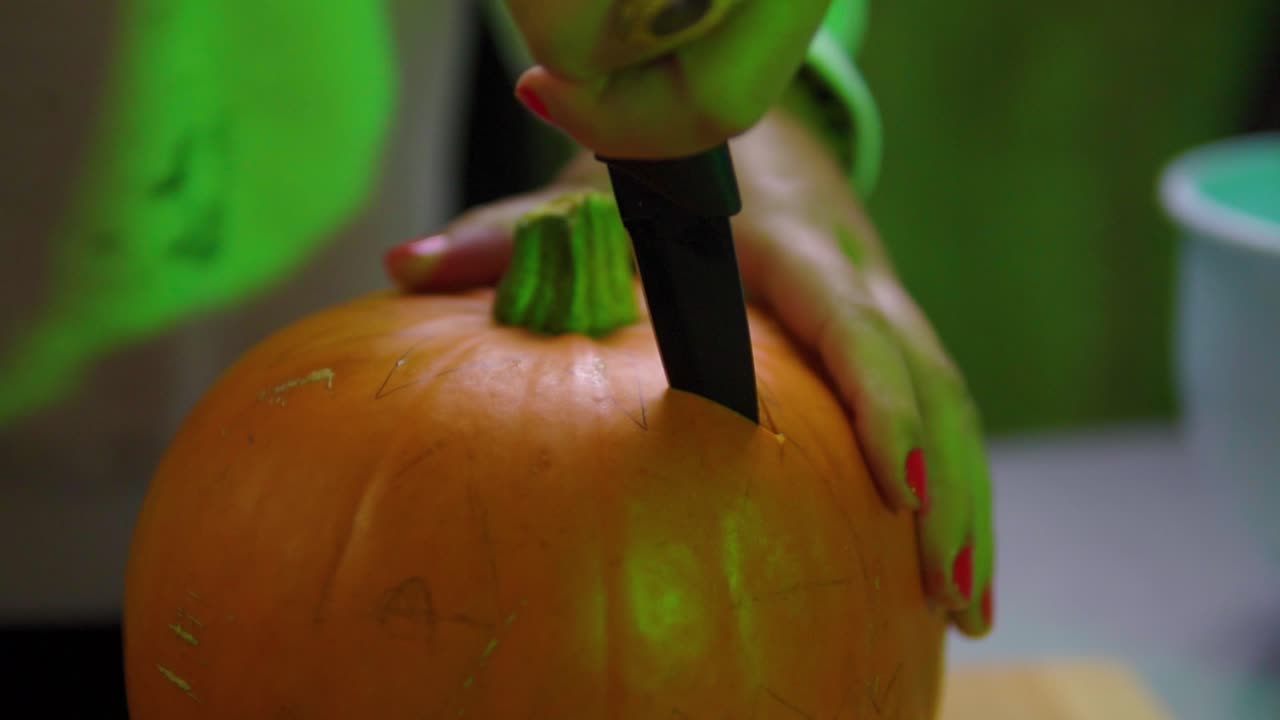 Carving a small pumpkin inside the house surrounded by green light looking spooky