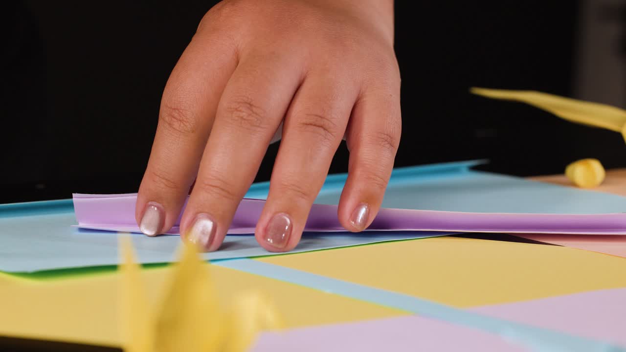 Primo piano di mani che piegano carta viola su una scrivania colorata con illuminazione soffusa
