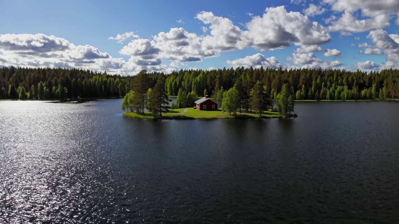 Aerial video captures a serene island with a red cabin surrounded by lush forest and calm waters