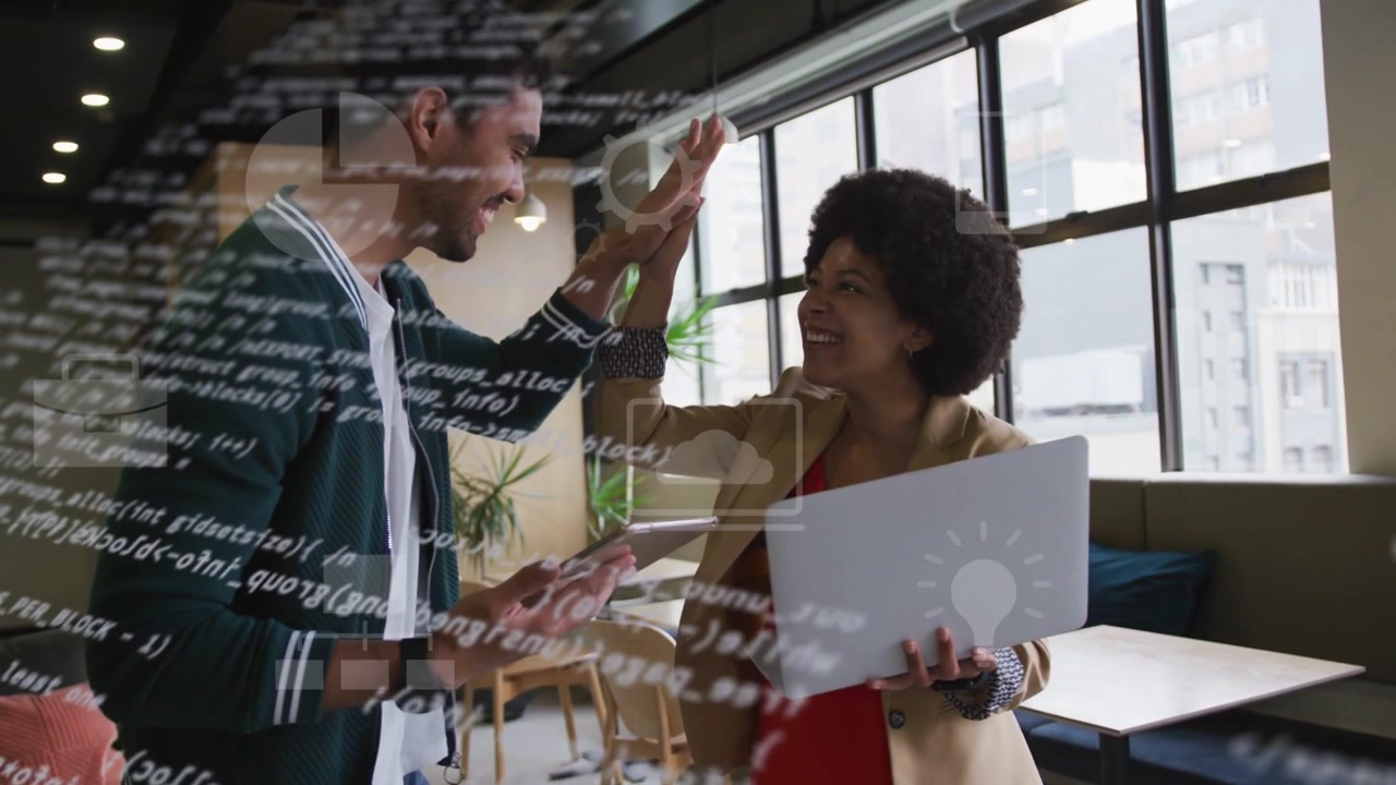 IT pair tapping tablet, scrolling laptop in lounge, code icons over screens leading high-five cheer
