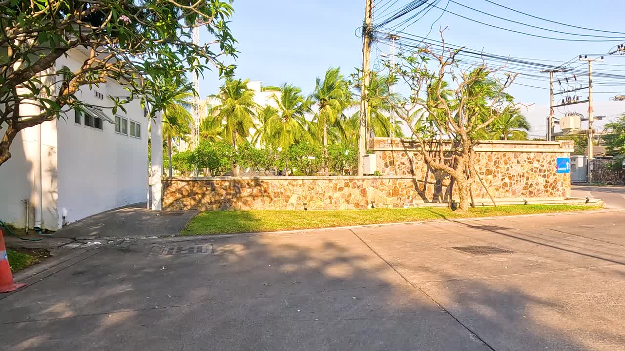 A serene street scene with palm trees and stone walls under bright sunlight in Chonburi, Thailand
