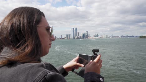 un primer plano de una mujer joven tomando videos con su teléfono inteligente de la orilla de nueva york desde el ferry de staten island