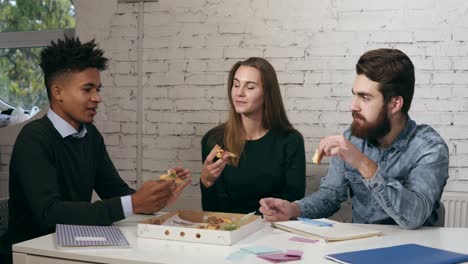 equipo de negocios de jóvenes alegres disfrutando de la pizza juntos en la oficina, están hablando divirtiéndose compartiendo el almuerzo en acogedor