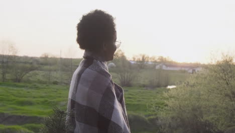 an young female contemplating the sunset in the forest covered by a blanket