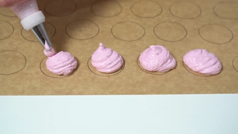 close up shot of baker using a pastry bag with macaron batter to fill up circular shapes on parchment paper.