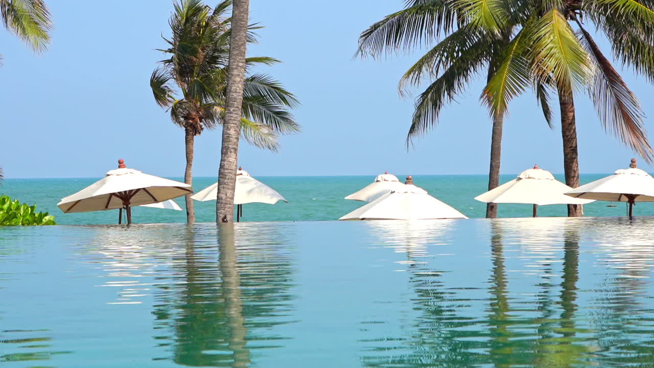 piscina de borde infinito y sombrillas blancas en la playa