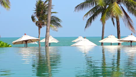 swimming edge infinity pool and white sun umbrellas on beach