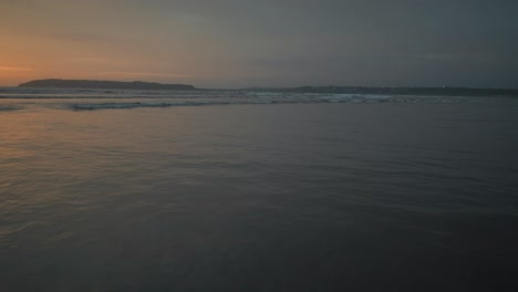 Seascape-view-of-ocean-waves-crashing-on-the-shoreline,-at-sunset,-on-a-cloudy-evening