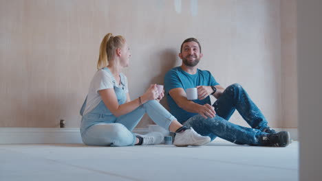 couple decorating room at home sitting on floor taking a break with hot drink