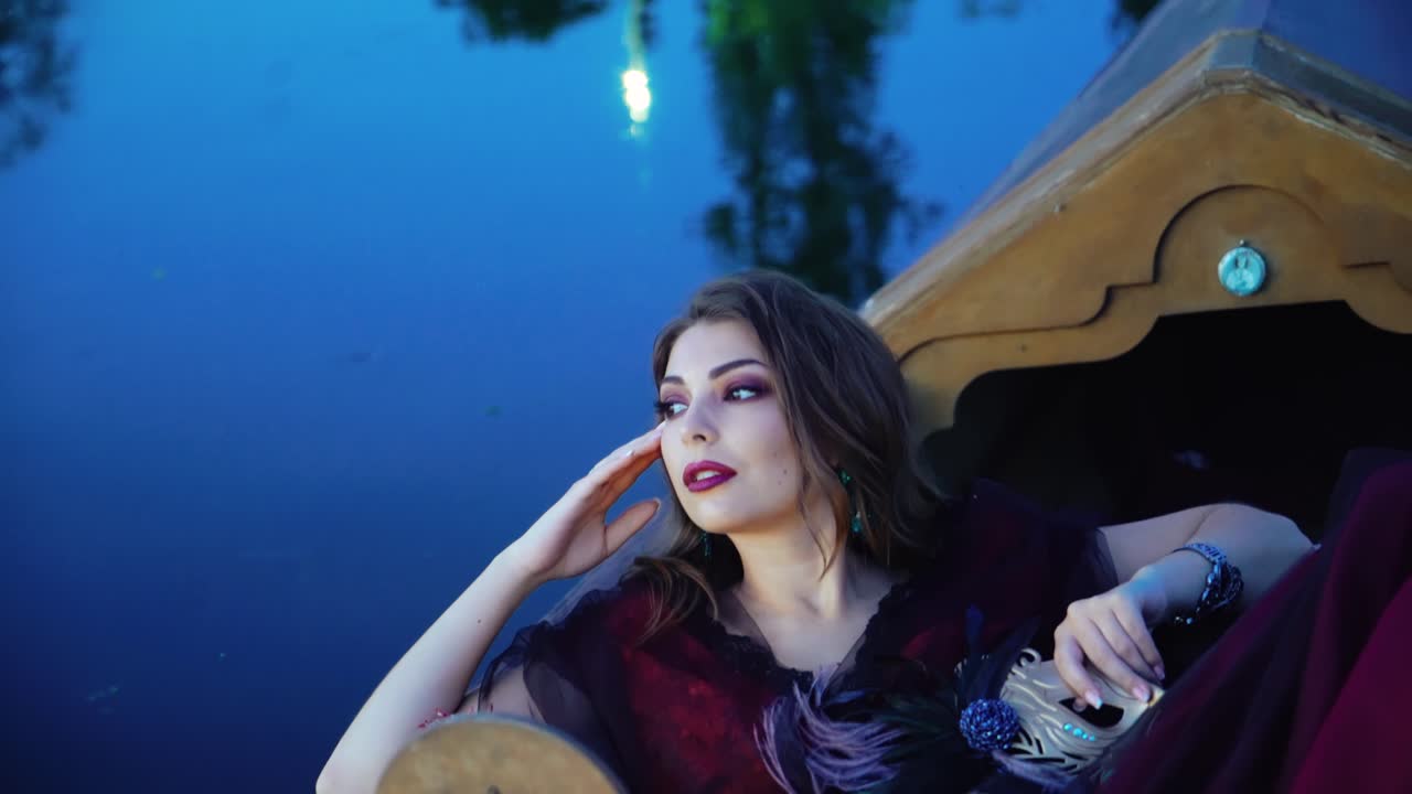 Attractive young woman with bright make-up lying in a boat at night and dreams about love. Sexy girl floating in a gondola on the blue water