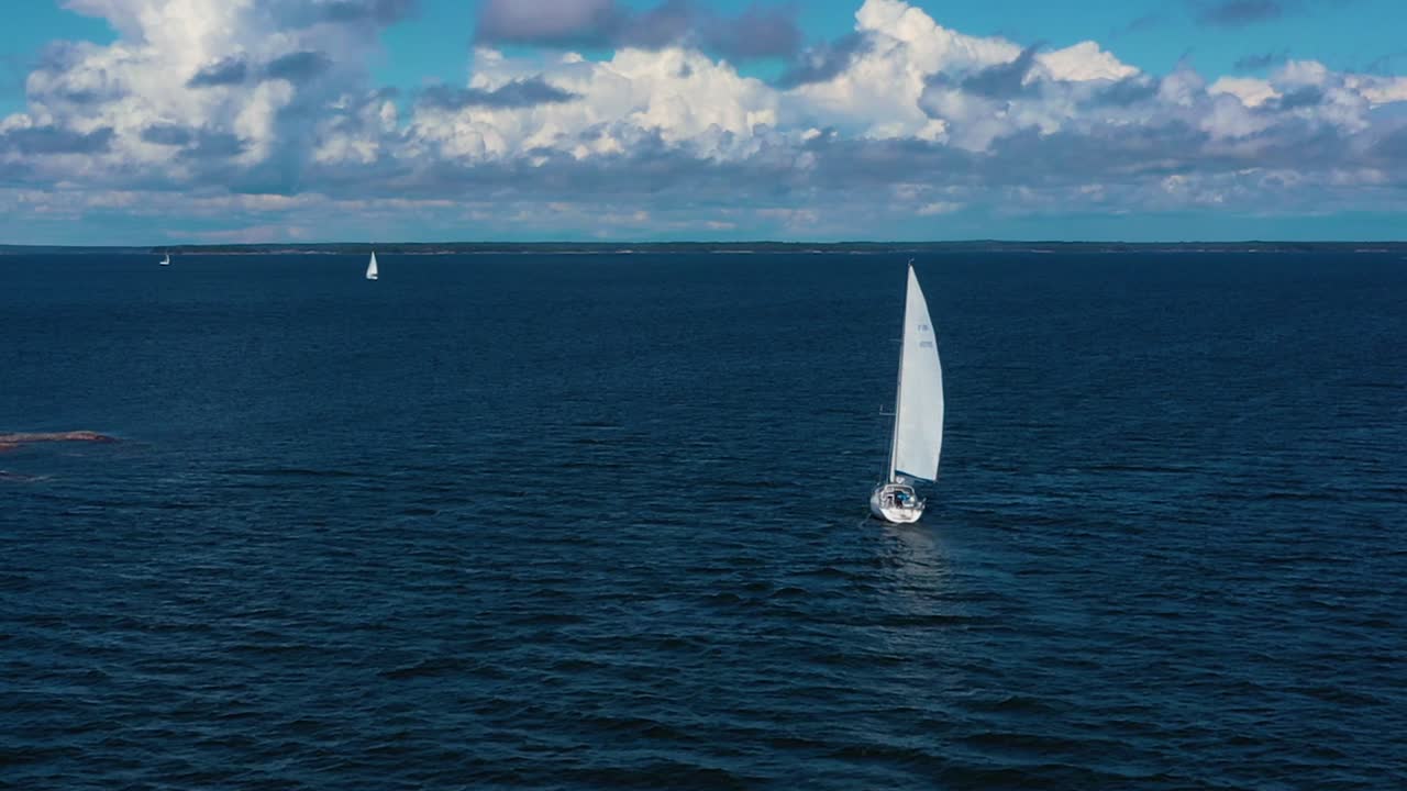 Aerial view following a white sailboat on the high seas, at the Baltic sea, bright, sunny, summer day, near Hanko, in Uusimaa, Finland - low, dolly, drone shot