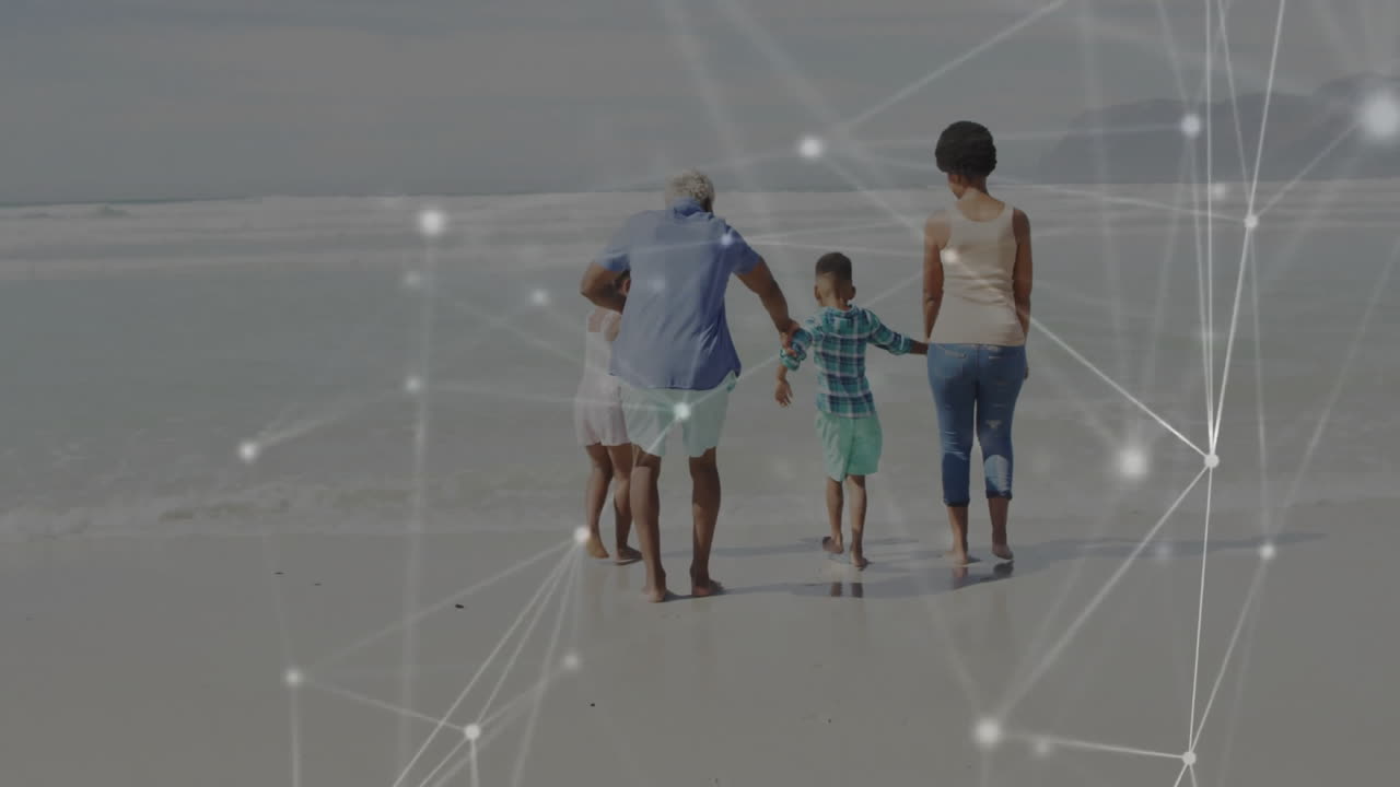 Family holding hands walking barefoot on wet sand toward waves, showing technology network overlay