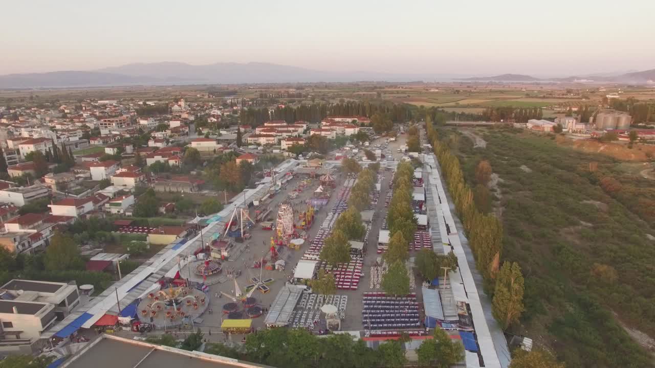 AERIAL drone footage of an amazing street market place bazaar and a fun luna park small town at background  and green trees sunrise summer day fun activities