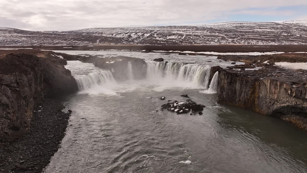Drone view of Goðafoss waterfall flowing through rugged terrain near Laugar, Iceland.