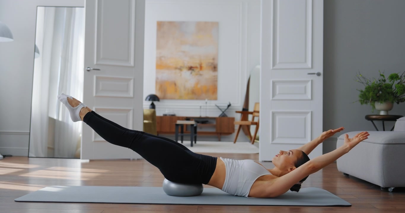 Giovane donna che esegue esercizi di Pilates con la palla su tappetino da yoga a casa