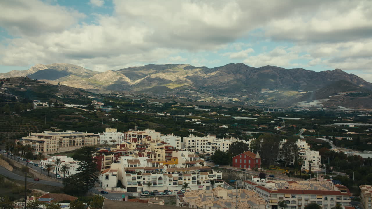 High-angle view from Salobreña castle showing white Andalusian town, rural valley and majestic Sierra Nevada mountains under clouds