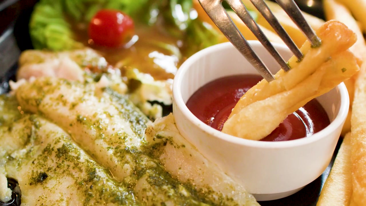 Primo piano di una forchetta che intinge una patatina fritta dorata in una ciotola di ketchup