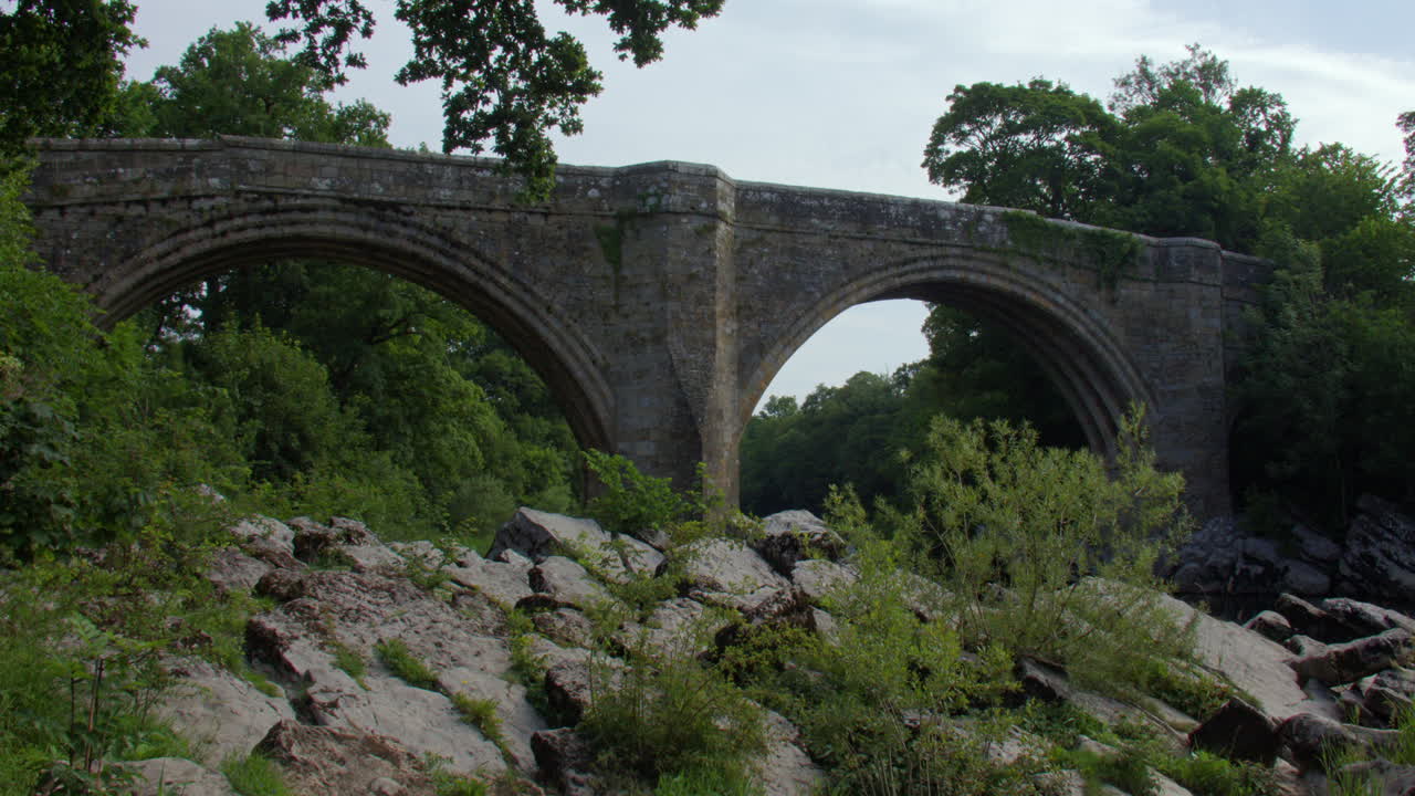 Tilting up shot looking up to devils bridge from the river Lune with rocks in foreground at Kirkby Lonsdale, North Yorkshire