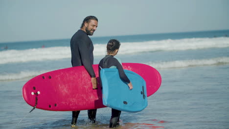 entrenador de surf con pierna artificial y chica sosteniendo tabla de surf y hablando mientras camina por la playa