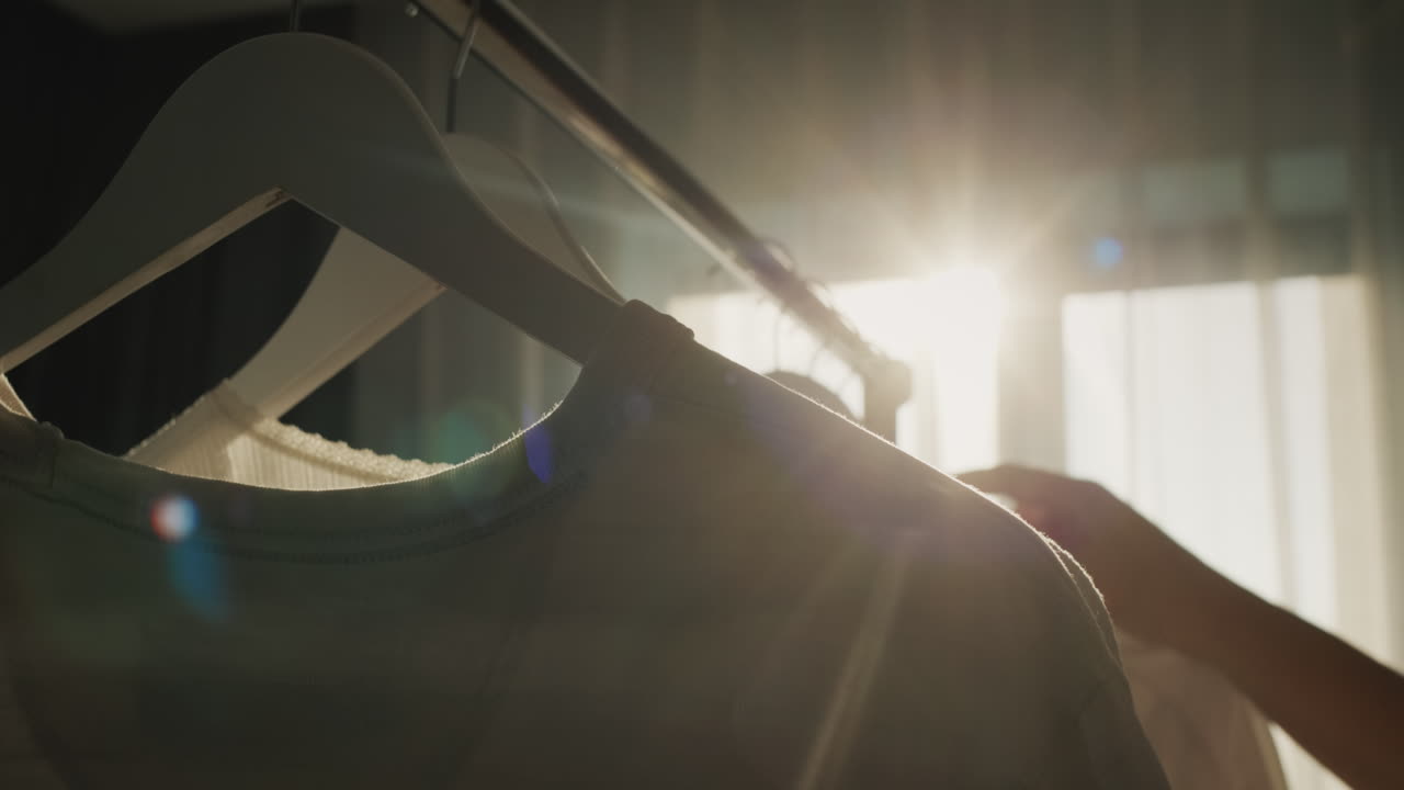 una mujer cuelga ropa en un estante, su silueta ilumina bellamente el sol desde la ventana