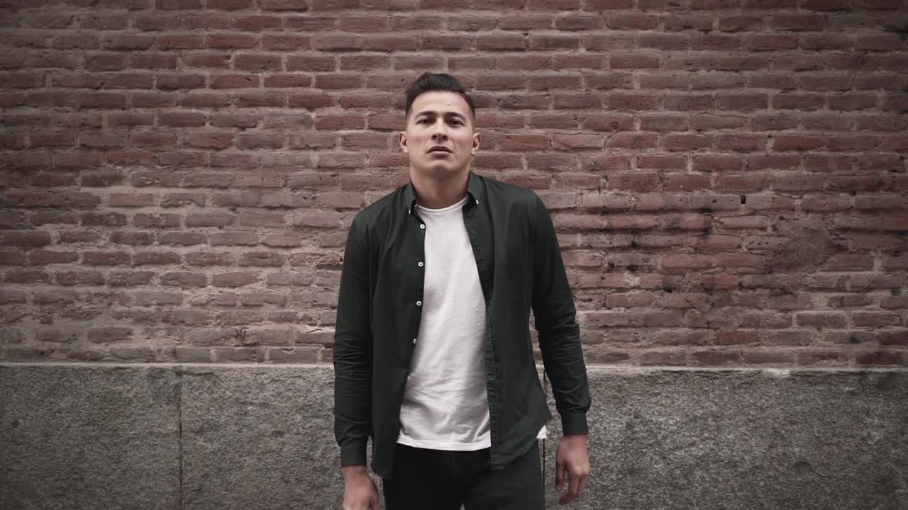 Man in a stylish casual outfit leaning against a brick wall