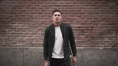 man in a stylish casual outfit leaning against a brick wall